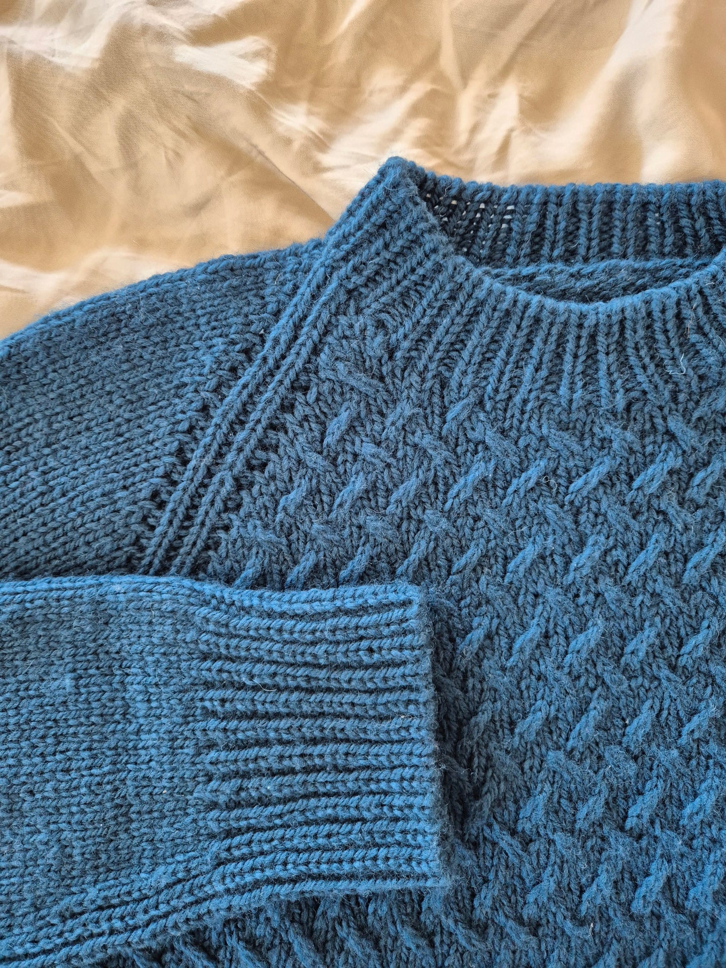 Close-up of a blue texture knitted handmade sweater on a beige fabric background