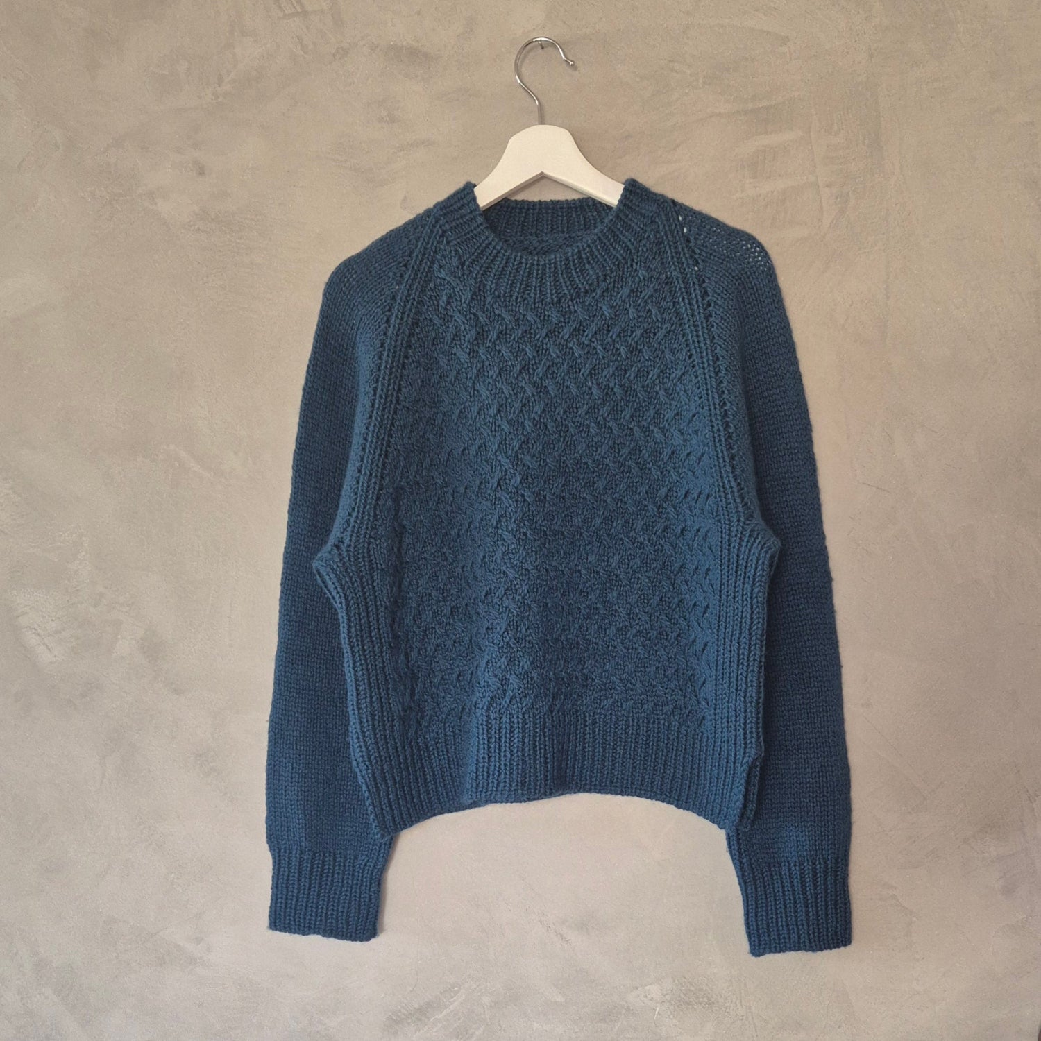 Blue Nordic style texture knitted sweater on a hanger against a gray wall.