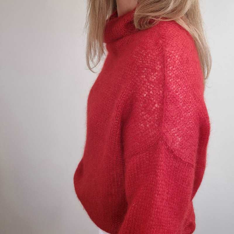 A woman wearing an elegant red, silk mohair, knitted sweater with an interesting shoulder construction.