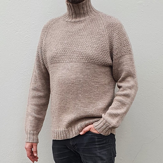 A man wearing a beige, high-collared, long-sleeved Duggari sweater, standing against a neutral background.