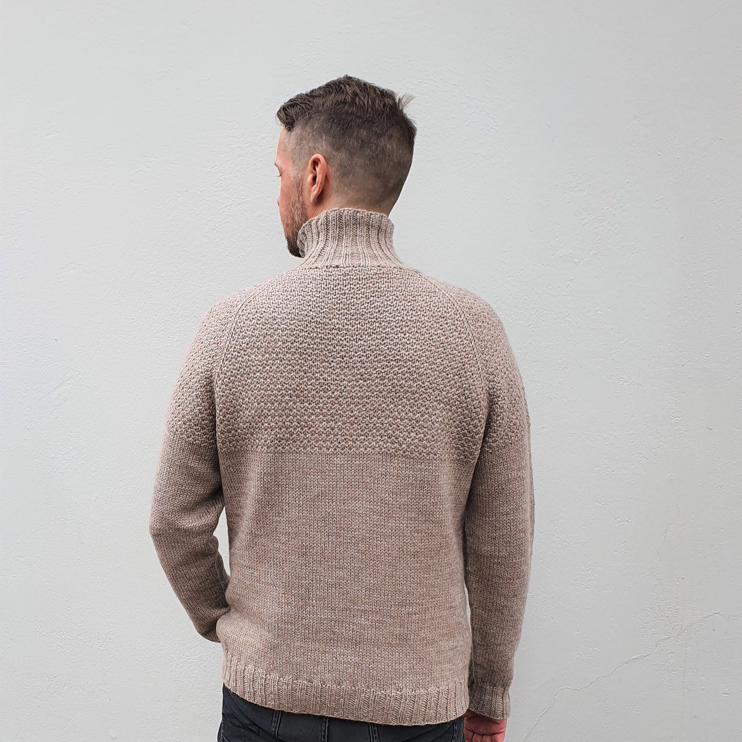A man wearing a beige, high-collared, long-sleeved Duggari sweater, seen from behind