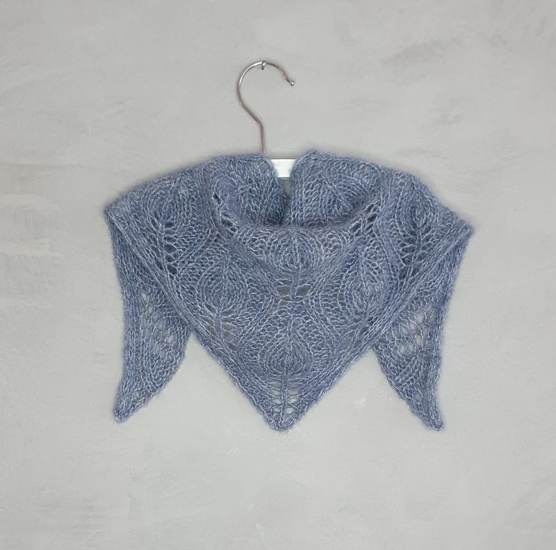 A small blue Nordic style hand knitted scarf with a flowing leaf pattern, draped over a white hanger.