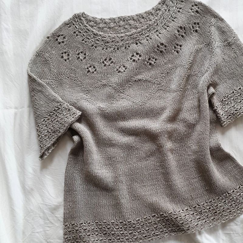 A short-sleeved, knitted top with a round neckline and decorative eyelets on the yoke, displayed on a neutral background.