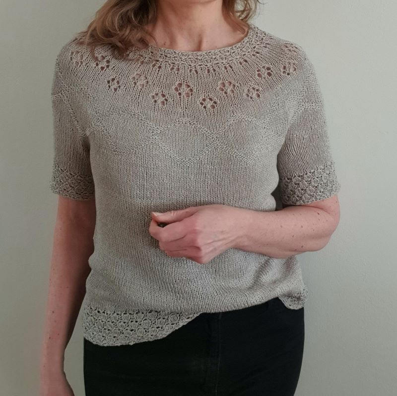 A woman wearing a short-sleeved, knitted top with a round neckline and decorative eyelets on the yoke.