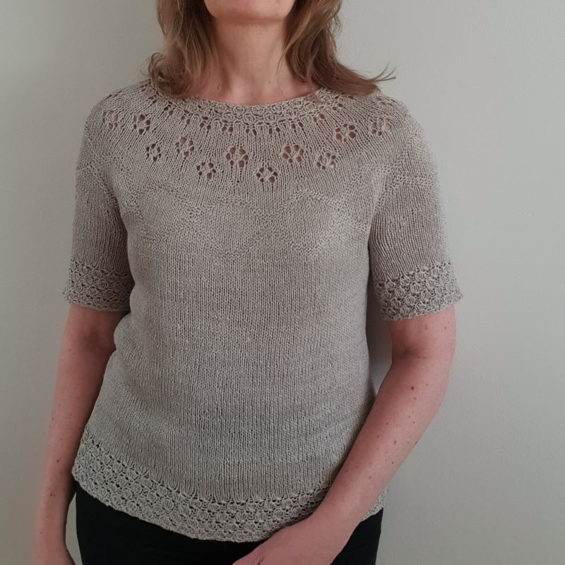 A woman wearing a short-sleeved, knitted top with a round neckline and decorative eyelets on the yoke.