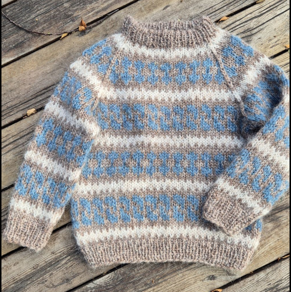 A Nordic style lopapeysa hand-knit toddler sweater with horizontal motive stripes in light blue, cream, and taupe, laid flat on weathered wooden planks.