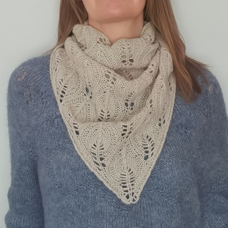 A woman wearing a Nordic style light beige cashmere hand knitted scarf with a flowing leaf pattern.