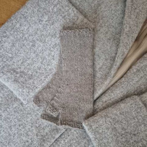 A close-up of gray-brow wrist warmers knitted in the round, showing the texture and a section of the knitting pattern.