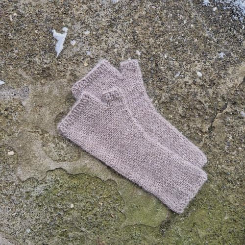 A pair of gray-brow wrist warmers knitted in the round, on concrete background.